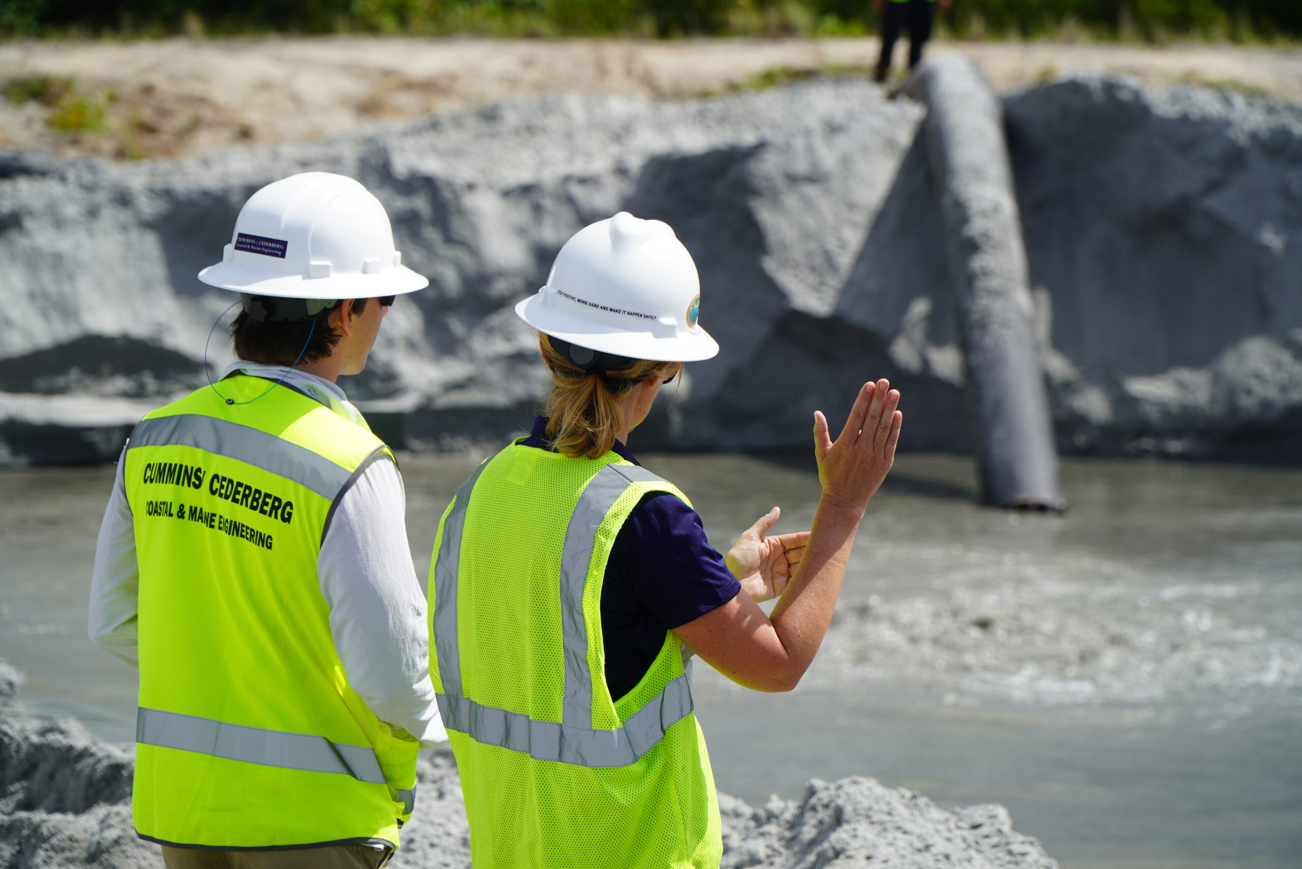 Two Cummins Cederberg team members in hard hats and safety vests reviewing a coastal work site