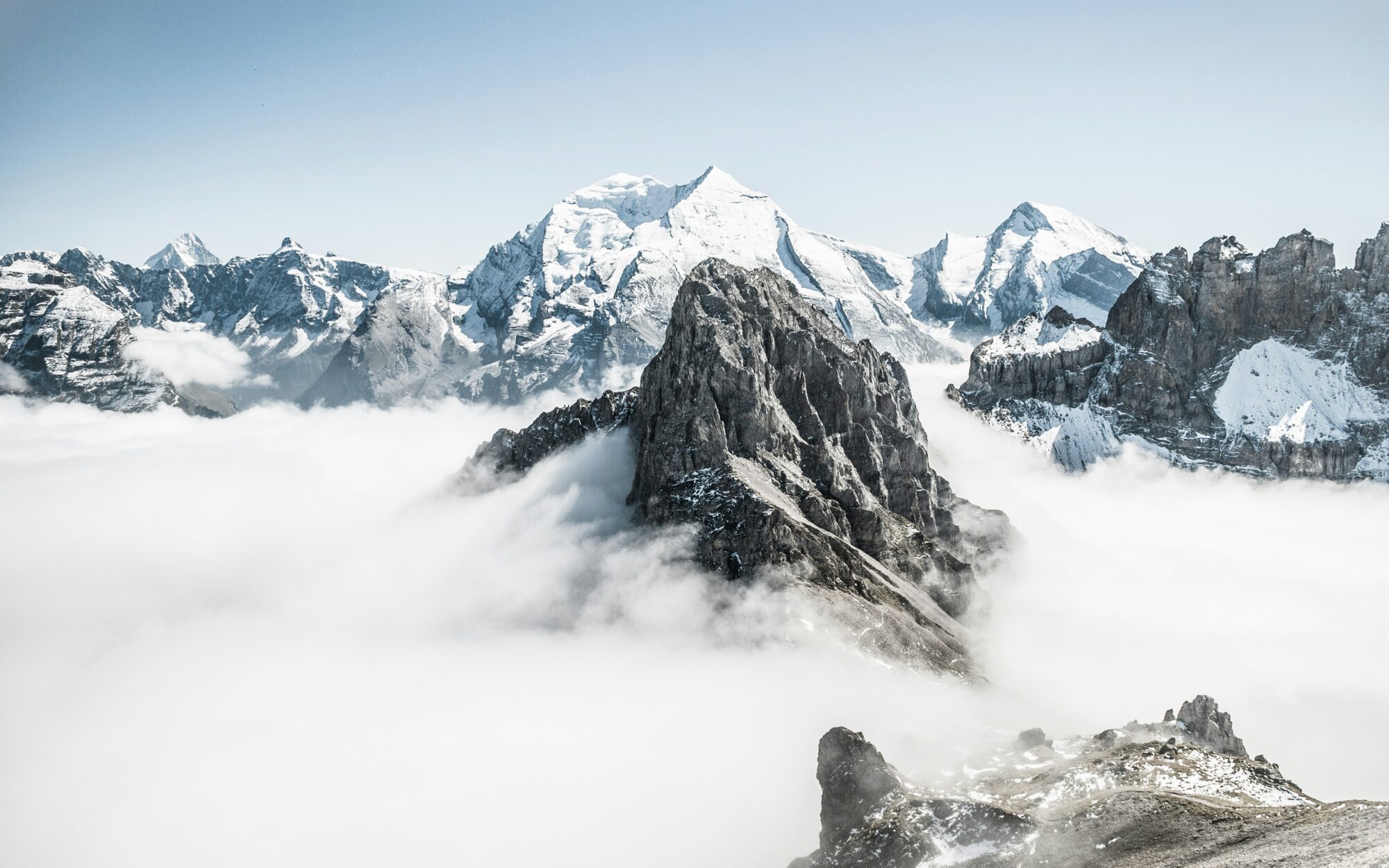 Snowy mountain peaks emerging from clouds under a clear sky